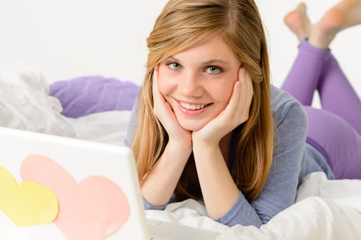 Young smiling girl lying on bed with laptop