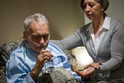Senior man taking medication with water caring wife helping