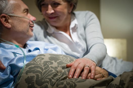 Elderly couple holding hands sick man lying in bed