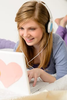 Young teenage girl chatting on laptop and lying on bed