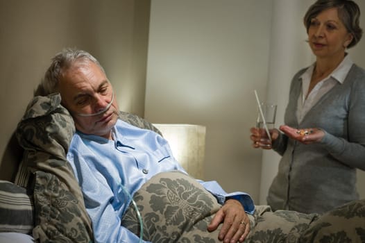 Ill old male patient and caring wife holding pills