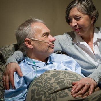 Seriously ill old man lying in bed with loving wife