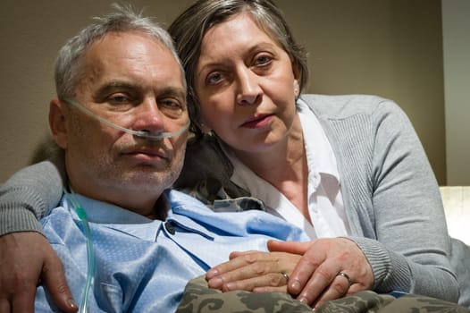 Anxious senior wife holding her sick husband at clinic