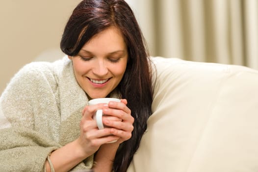 Smiling woman enjoying hot tea sitting on couch
