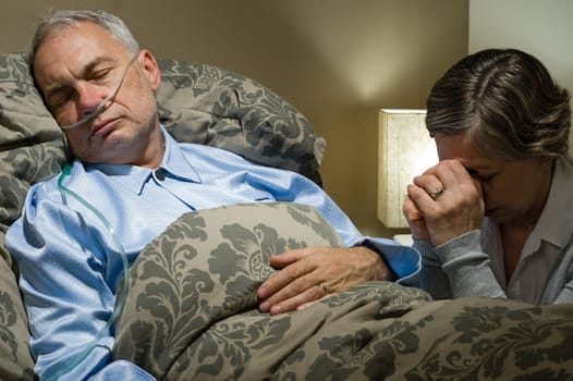 Senior woman praying for her sick husband lying in bed