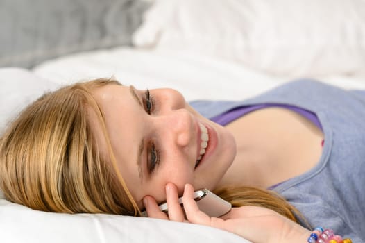 Lying joyful teenager girl talking on her phone in bed
