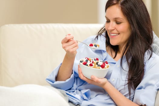 Young smiling woman eating healthy cereal lying on couch