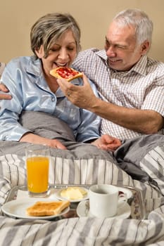 Senior couple lying in bed man feeding breakfast to woman