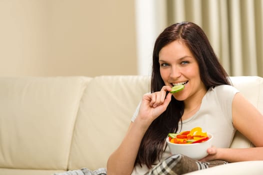 Woman sitting on sofa eating colorful mixed salad