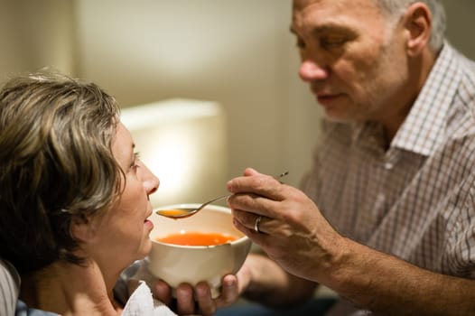 Caring senior man feeding his sick wife with warm soup