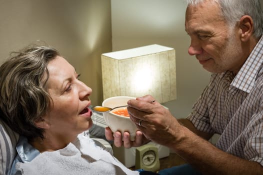 Loving retired husband feeding his ill wife with soup