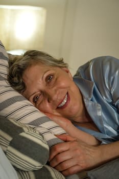 Retired smiling woman lying in bed looking at camera