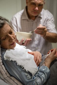 Mature man helping his ill wife feeding soup