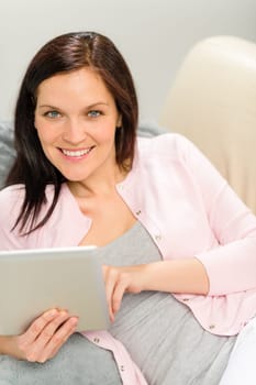Beautiful joyful woman holding digital tablet lying on couch