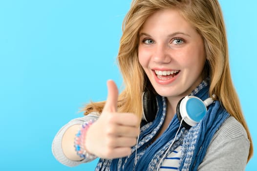 Cheerful teenage girl showing thumbs up isolated on blue background