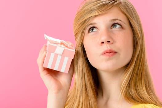 Curious girl holding unopened present isolated on pink background