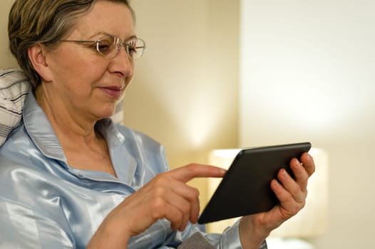Senior woman using digital tablet lying in bed