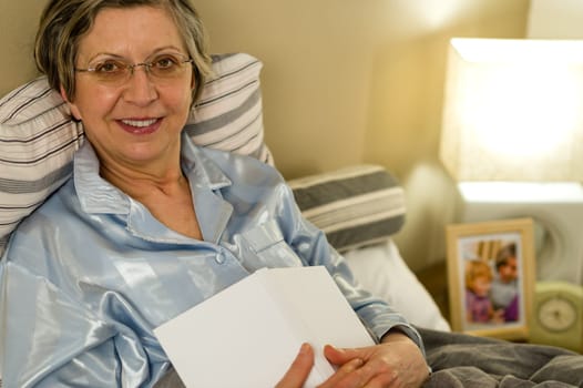 Old woman in pajamas lying in bed looking at camera