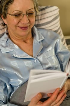 Elderly smiling woman reading book lying in bed