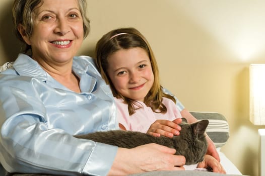 Cheerful senior woman with granddaughter and cat lying in bed