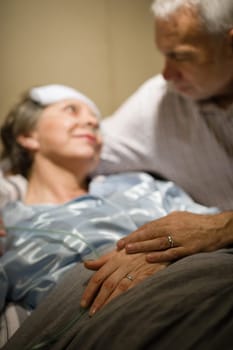 Elderly couple holding hands at clinic ward bed