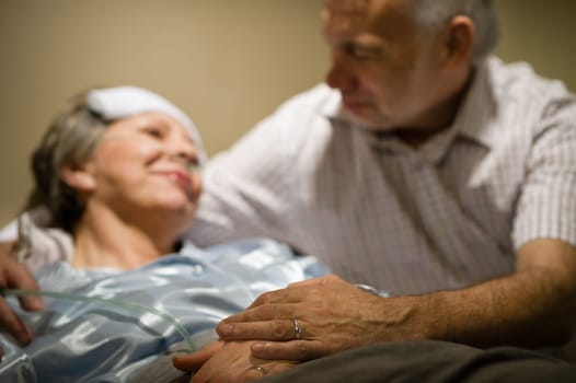 Old woman in pain lying bed holding hands with husband