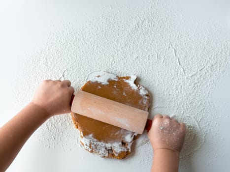 Child rolling dough with flour on white surface.