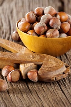 Hazelnuts in a wooden bowl with a wooden nutcracker on a rustic wooden surface