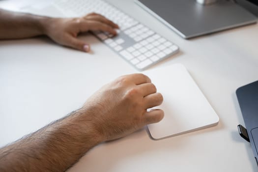 Close up of male hands using white keyboard and trackpad in office setting.