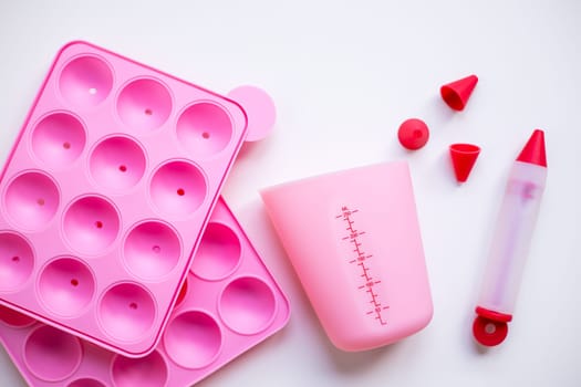 Pink baking utensils set with silicone molds and measuring cup on white background.