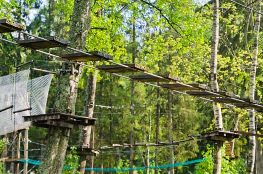 Dangerous ropeway with tether in rope park, trees with green leaves