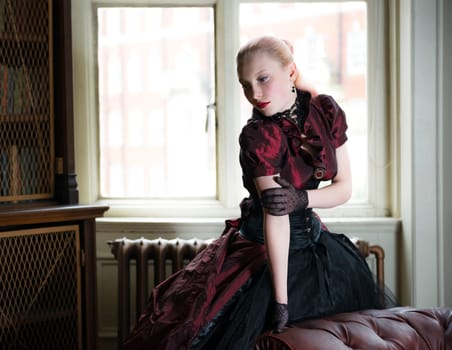 Beautiful caucasian woman in red Victorian dress waiting in old library