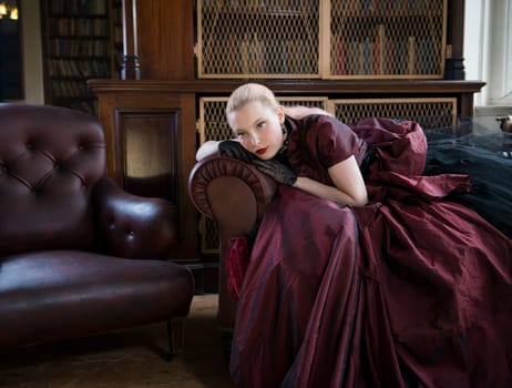 Beautiful caucasian woman in red Victorian dress waiting in old library
