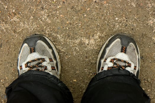Photo of feet in sports footwear against soil