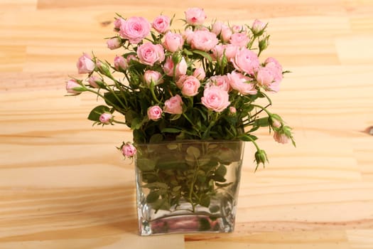 Bunch of small pink Roses in a glass vase over a wooden table.