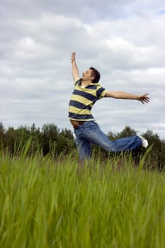 The young man joyfully jumps on a grass