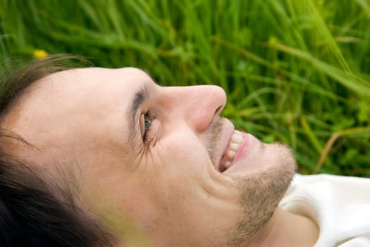 The man lies on a grass and smiles