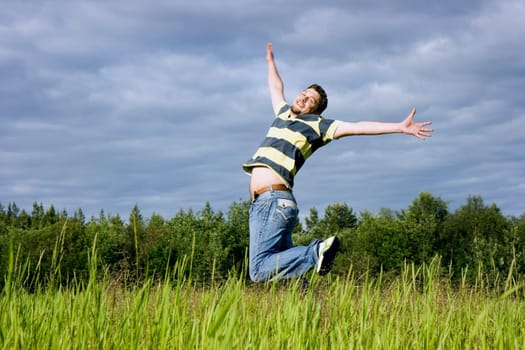 The young man joyfully jumps up in a grass