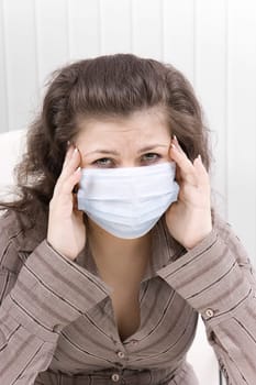 The young woman with sad eyes in medical mask keeps for sick head