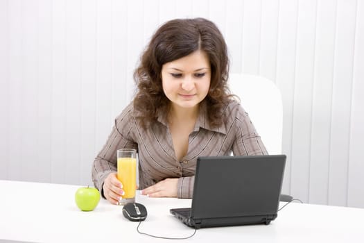 The laptop on table. The business girl at job. Glass with juice and apple.