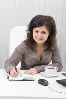 The young brunette works at office writing down in notebook