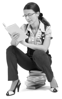 young girl with glasses sitting on a pile of books and reading