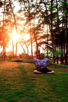 Vertical color portrait of man laying on garden lawn, arms acting as support for head, point of view at his head, kness folded up, sunset shininng through the trees, location of shot Manori, Bombay, India