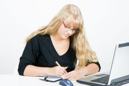 blonde girl with a laptop writes in a notebook