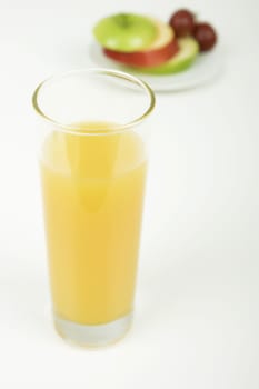 a glass of orange juice. A plate of fruit in the background