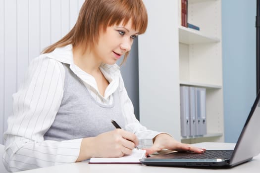 attractive young woman working with laptop on a background of office interior
