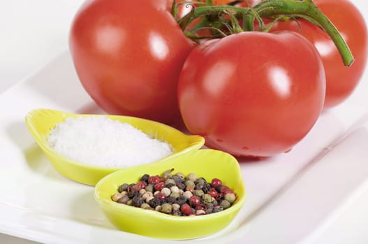 Fresh vine tomatoes with a bowl of fleur de sel and a bowl of peppercorns