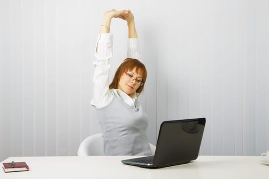 tired girl with a laptop stretches in the workplace