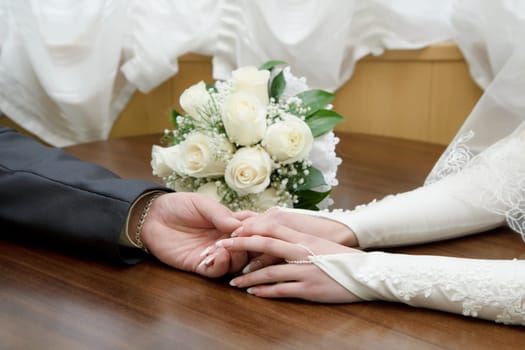 hands of the bride and groom on the background of a wedding bouquet