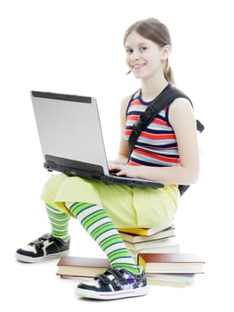 Teen girl smiling in a summer dress with a laptop sitting on the books. White background